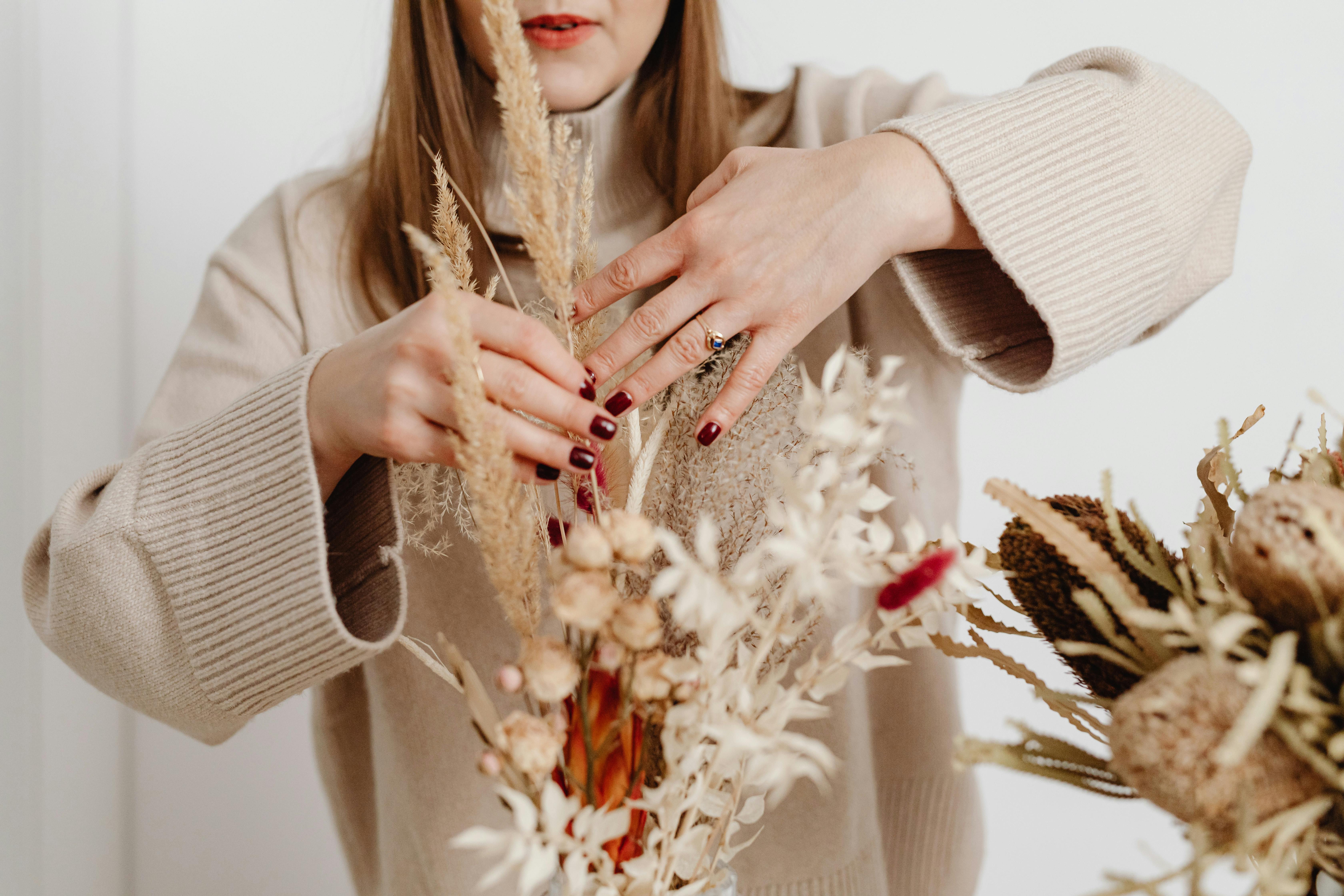 Woman arranging dried flowers in a cozy indoor setting, showcasing natural decor.