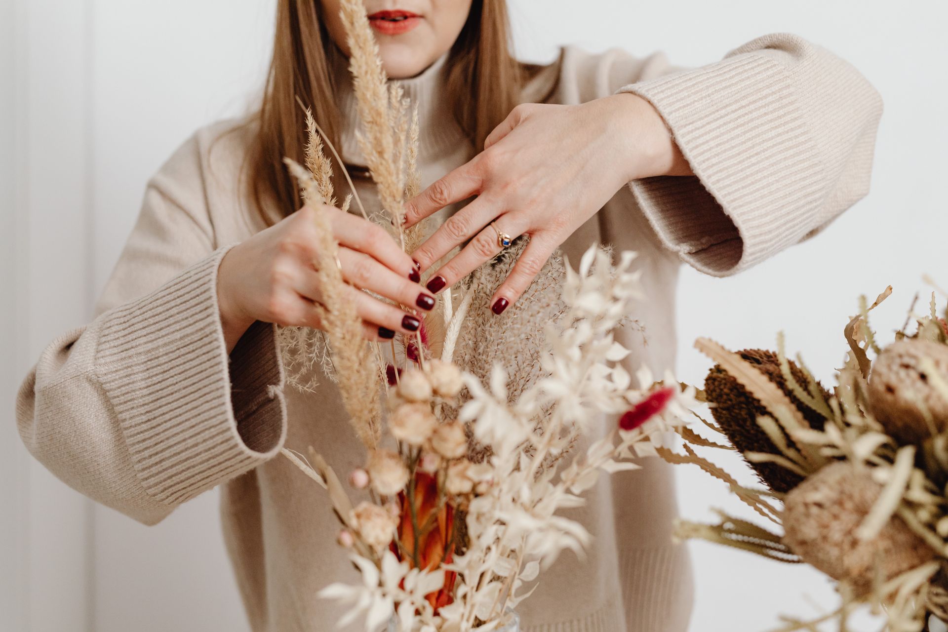 Woman arranging dried flowers in a cozy indoor setting, showcasing natural decor.