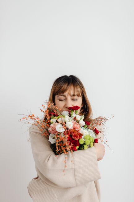 A woman with closed eyes embraces a vibrant bouquet of flowers against a white background.
