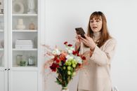 Woman in Beige Sweater Taking a Photo of Flowers