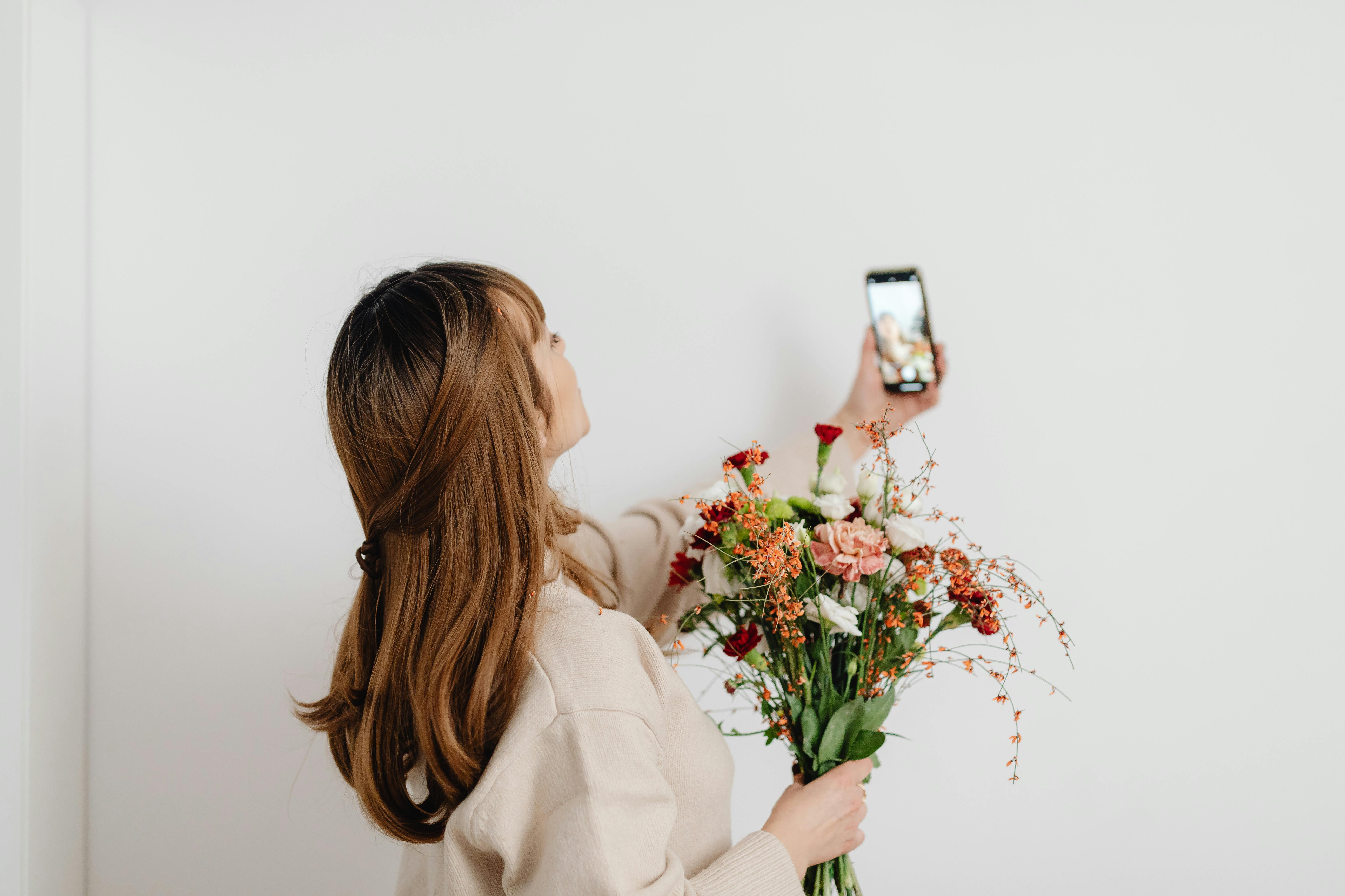 A woman takes a selfie with a colorful flower bouquet in front of a white background.