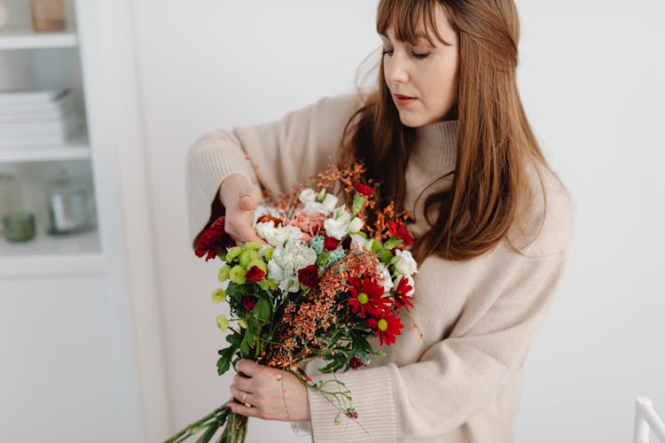 Redhead Woman Arranging Red And White Bouquet In A White Interior