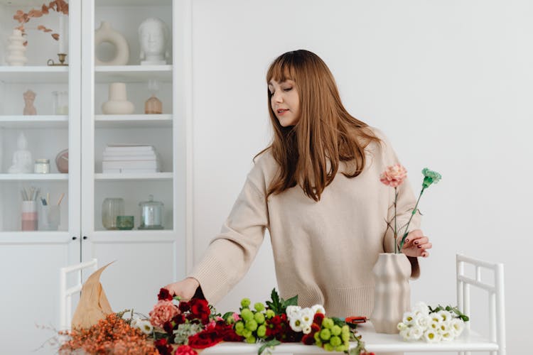 Woman In Beige Sweater Arranging Flowers In A Vase