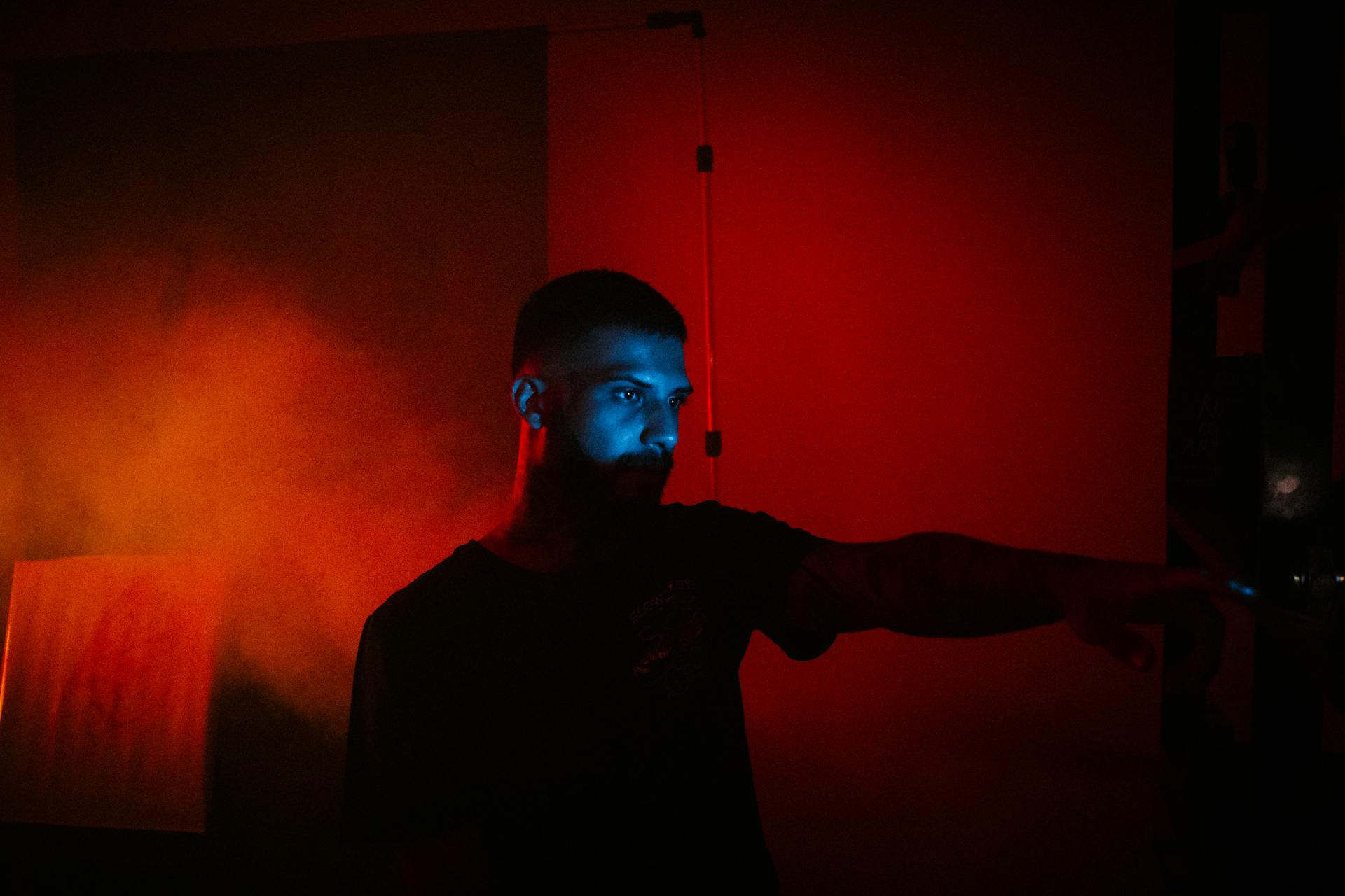 Concentrated male with eyes lightened by multimedia projector standing in dark room with red illumination