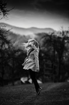 Black and white photo of a child joyfully jumping in a misty meadow, capturing movement and freedom.