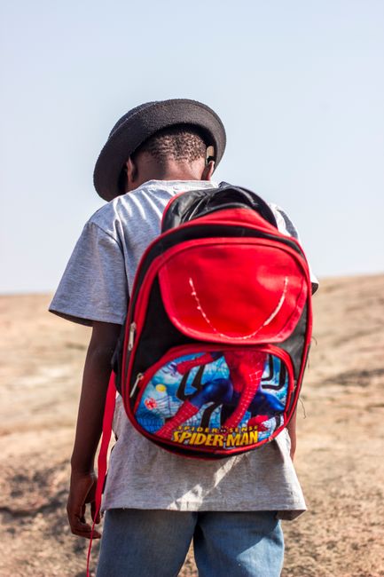 Back view of a child wearing a Spider-Man backpack, standing outdoors.