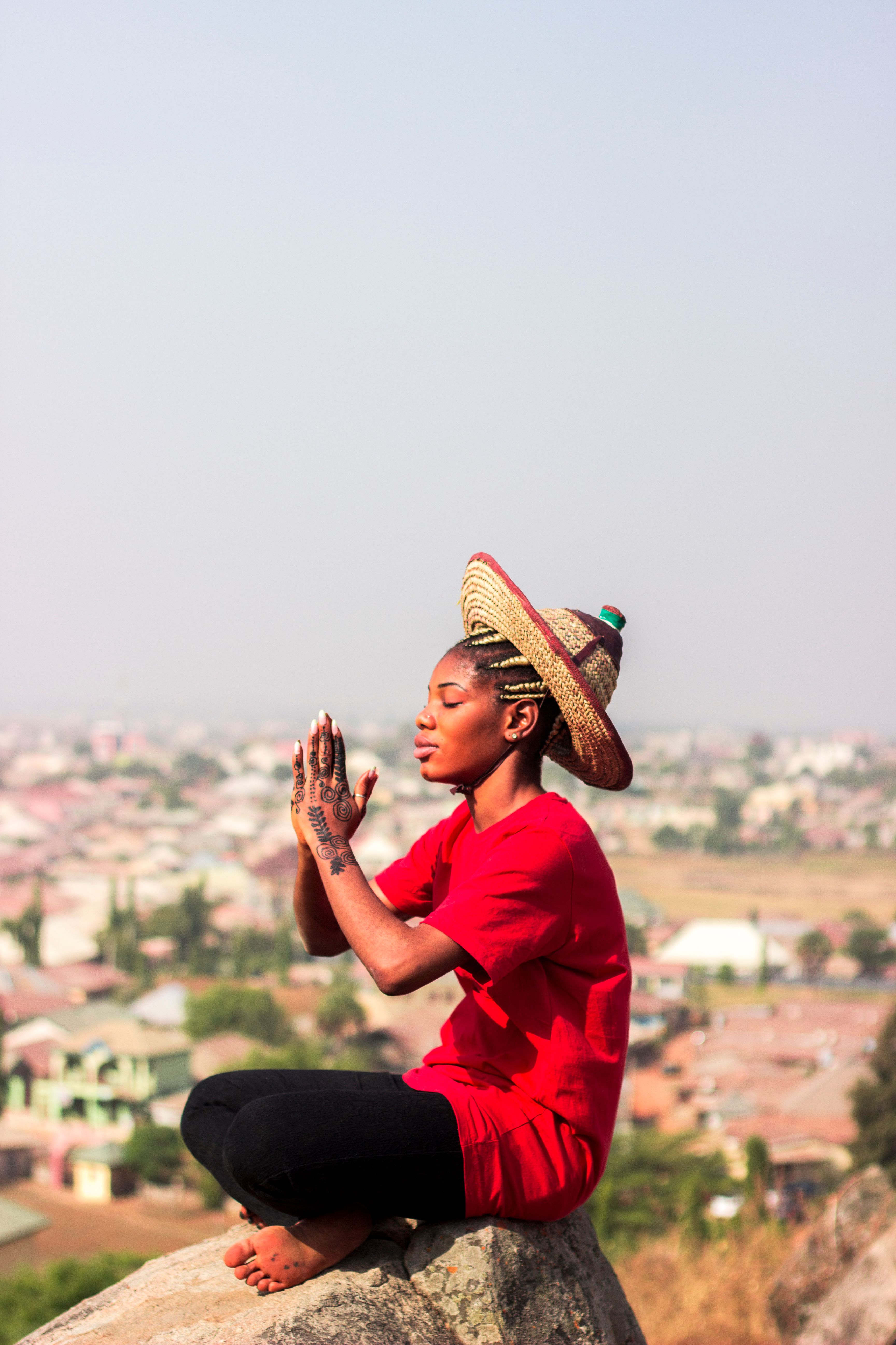 African woman with henna tattoo meditating on cliff edge with cityscape view.