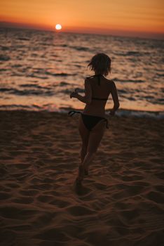 A woman in a bikini runs along the beach as the sun sets in Vietnam.