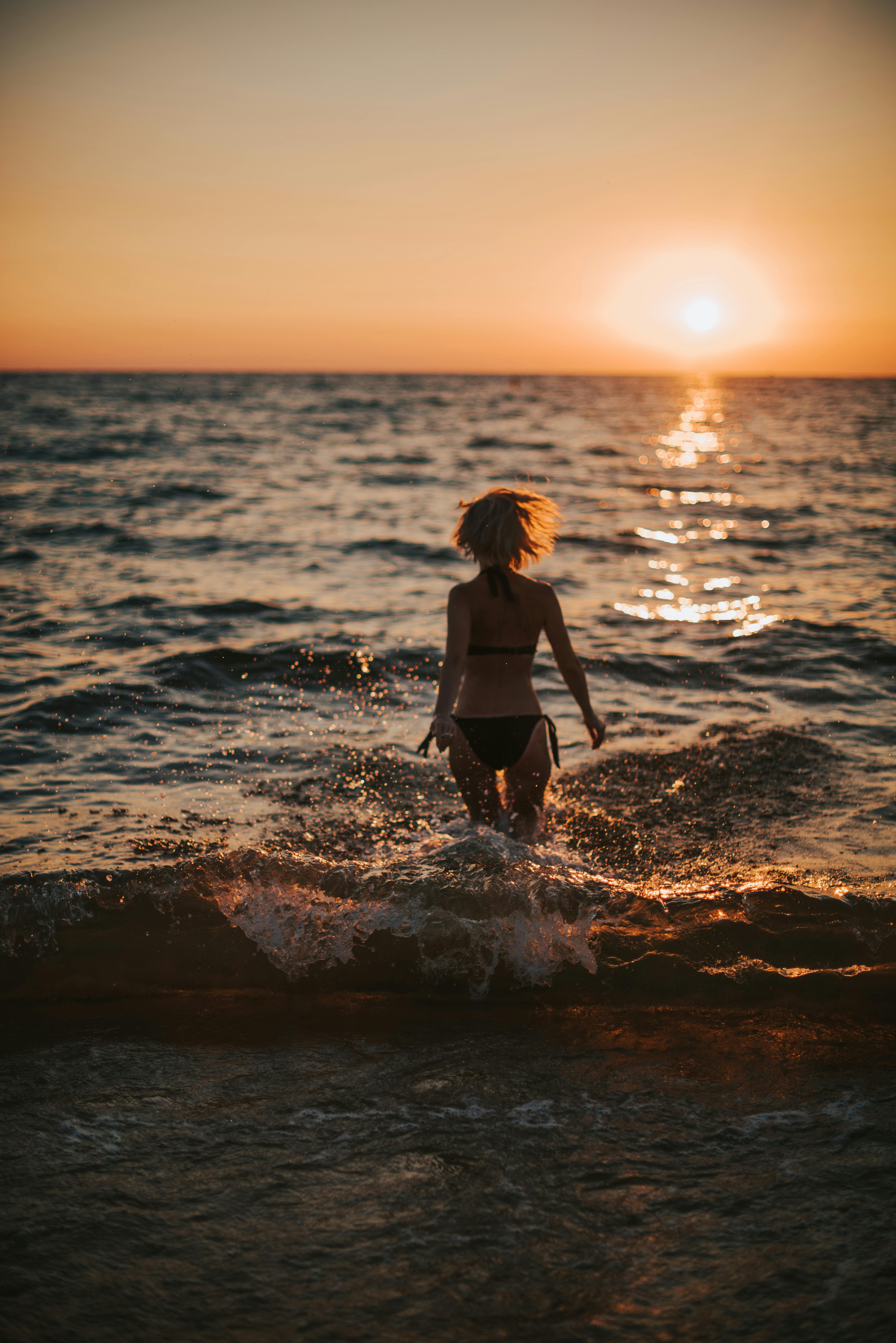Silhouette of a woman in a bikini running into the ocean during a breathtaking sunset.