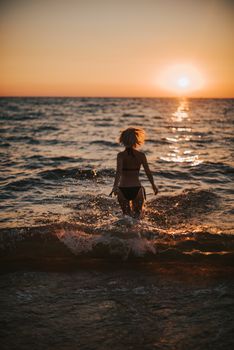 Silhouette of a woman in a bikini running into the ocean during a breathtaking sunset.