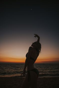 Elegant silhouette of a woman in a bikini dancing at sunset on a Vietnamese beach, capturing the serene ocean backdrop.