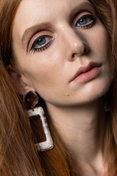 Intimate close-up shot of a woman with distinct red hair and unique earrings, conveying elegance and depth.
