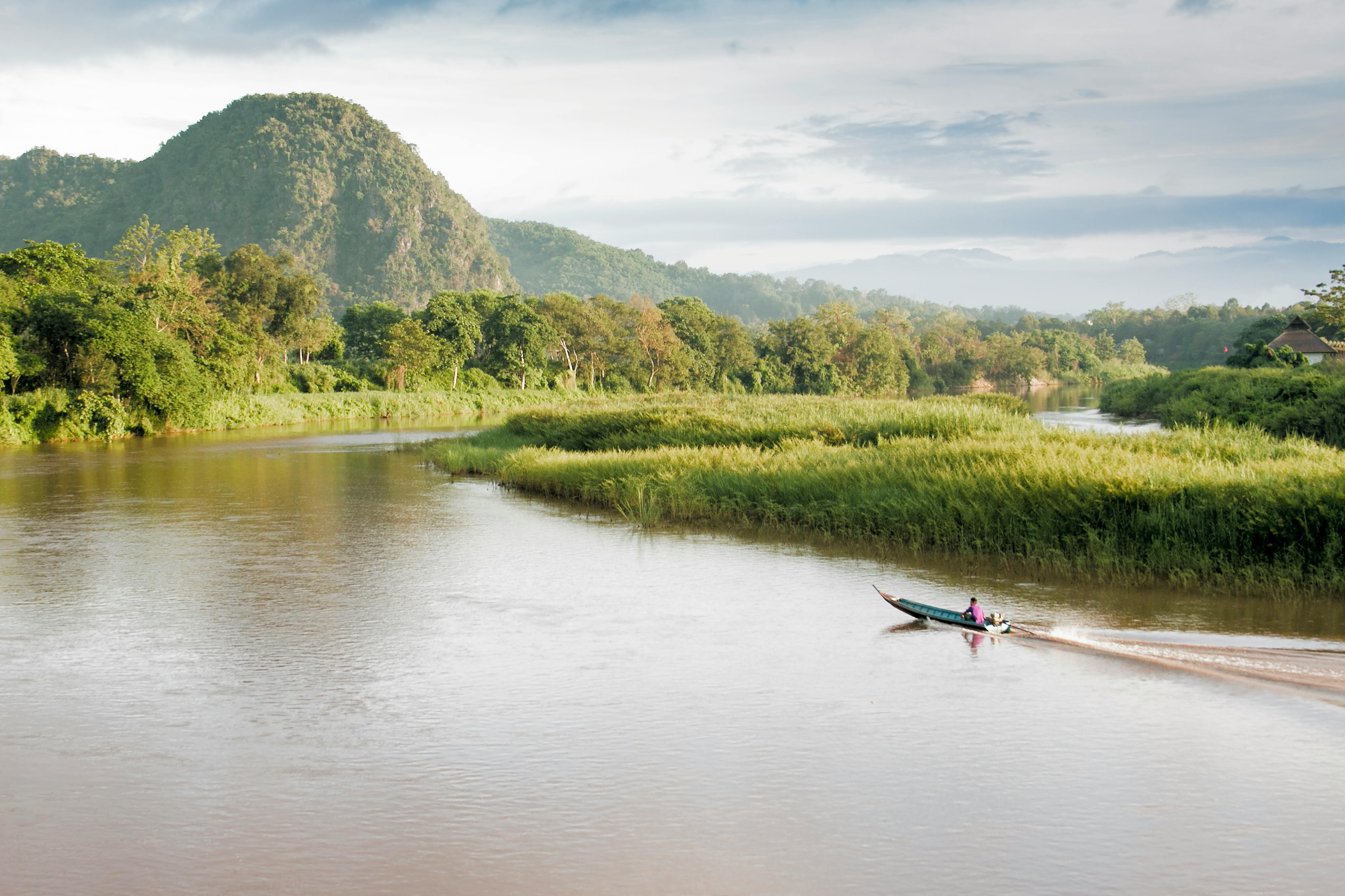 A tranquil river scene with motorboat in lush Chiang Rai landscape, Thailand.
