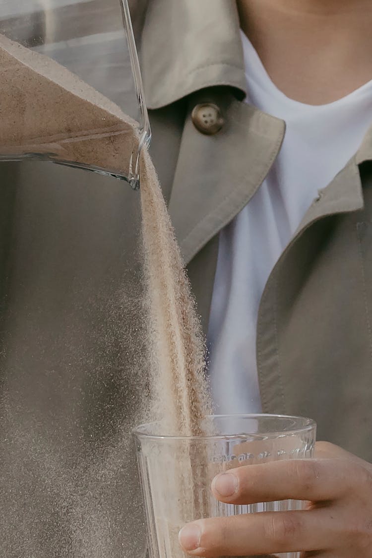 A Person Pouring Sand Into A Glass 