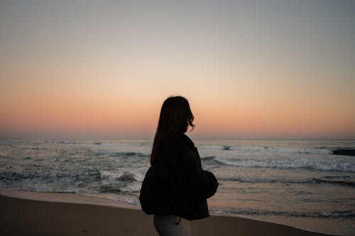 Free Silhouette of a Woman Standing on the Beach Stock Photo