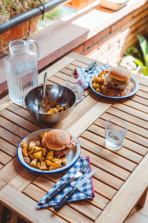Free From above of tasty homemade burgers on plate with roasted potato served on table with jug of water and tableware Stock Photo
