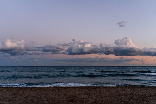 Free Vibrant sunset view of surfers enjoying the waves beneath a dramatic cloudscape. Stock Photo
