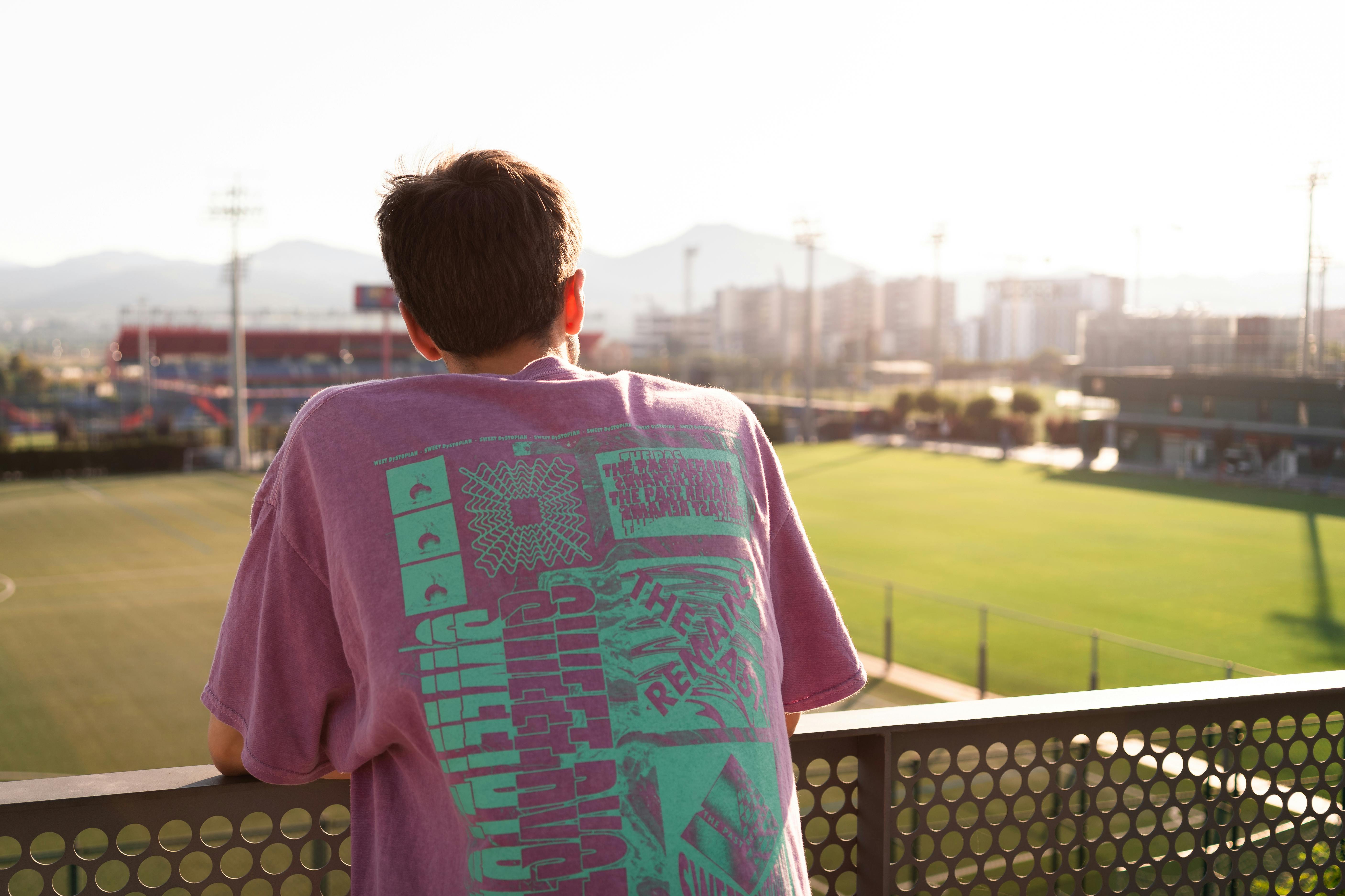 young man standing near fence and looking at play field