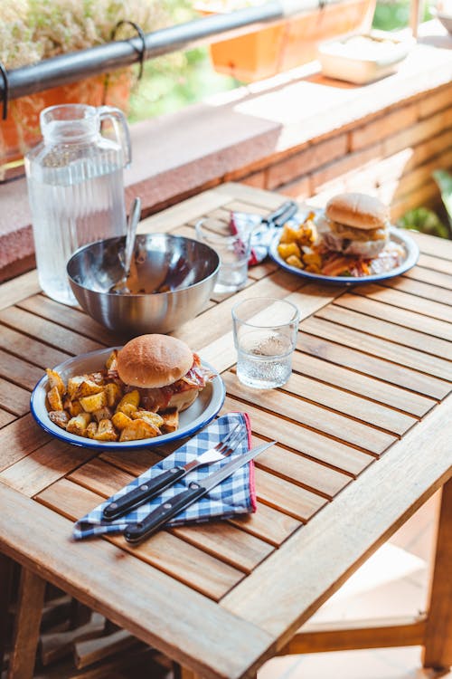 Free High angle of wooden table served with tasty homemade burgers on plates with roasted potato and jug of water Stock Photo