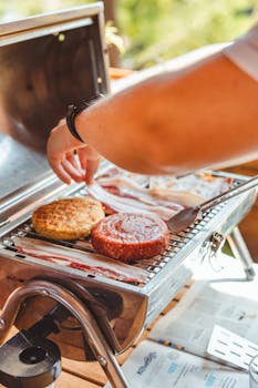 Person grilling burgers outdoors on a barbecue, perfect for summer picnics.