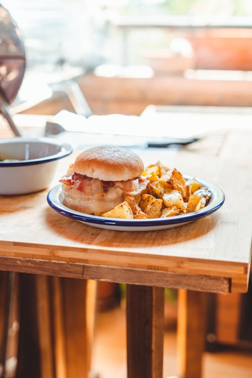 Free Plate with delicious fried potato and burger with bacon placed on wooden table in cafe Stock Photo