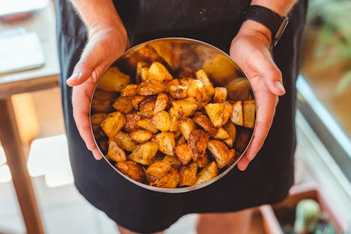 Free From above of crop anonymous male chef in apron standing with bowl of potato wedges Stock Photo