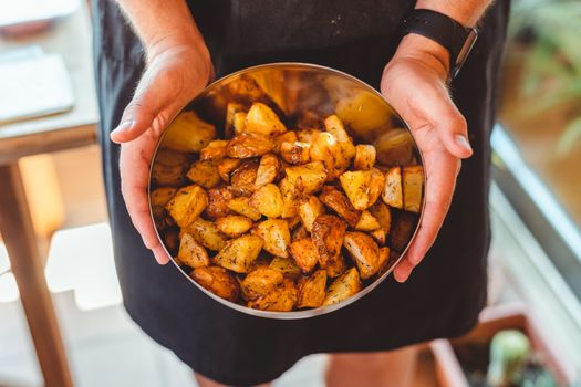 From above of crop anonymous male chef in apron standing with bowl of potato wedges