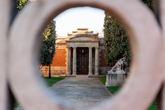 View through hole of gate on stone library with columns near sculpture in park