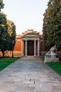 Paved walkway leading to historic building of library with columns located in park with trees and statue in Spain