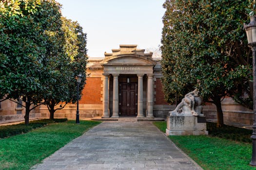Facade of old library with high columns with walkway and statue in green park in Spain