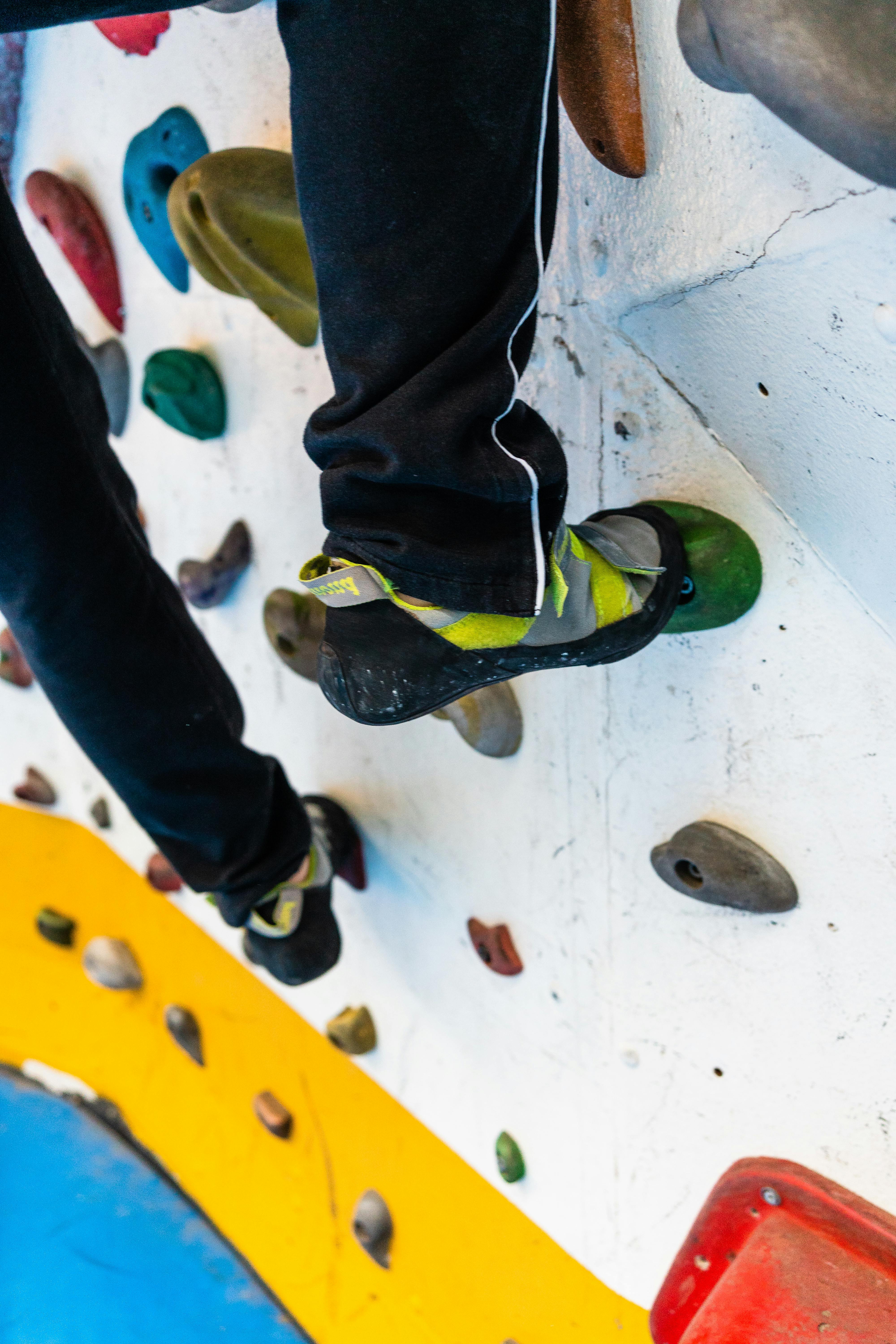 High angle of crop faceless climber standing on artificial boulder while ascending climbing wall