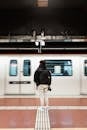 Full body back view of anonymous male standing on platform of subway station near moving train while waiting for transport on blurred background