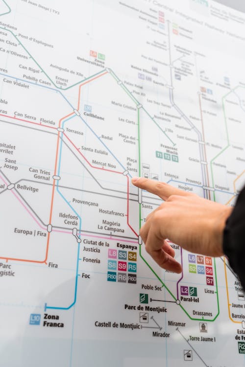 Unrecognizable person pointing at map of metropolitan station with various colorful underground lines while choosing route for ride on street