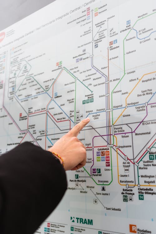 Free Unrecognizable person near information board pointing at map with colorful metro lines while choosing route for rise on street in city Stock Photo