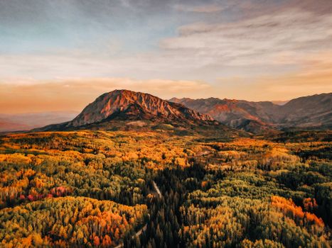 Stunning aerial view of a vibrant autumn forest with mountains in the background at sunrise.