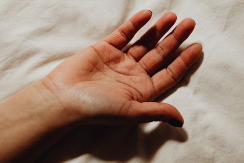 Free A close-up image of a human hand resting on soft white bedding, capturing skin texture. Stock Photo