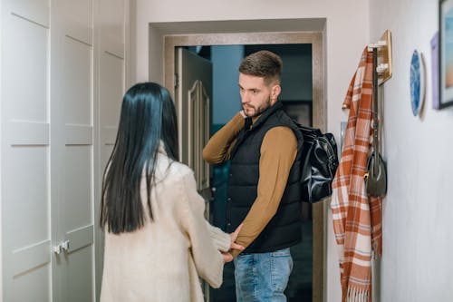 A Person in Cream Sweater Holding the Hand of a Man Near the Doorway