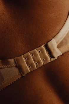 Detailed close-up shot of a beige bra hook and skin texture in warm lighting.