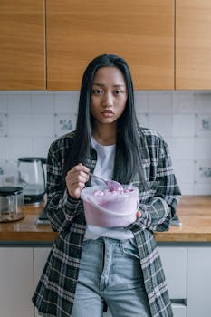 Asian woman holding a container of ice cream in a modern kitchen setting.