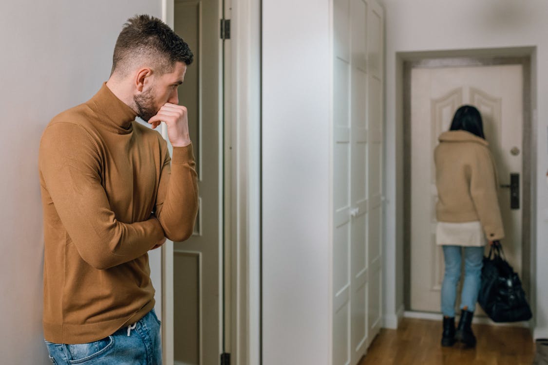Free Man in Brown Long Sleeve Shirt and Blue Denim Jeans Standing Near White Wall Stock Photo