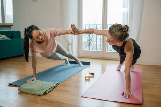 Two women performing yoga plank exercises on mats with a supportive high-five indoors.