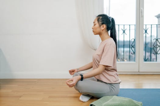 Asian woman meditating indoors on a yoga mat, exuding calm and serenity.
