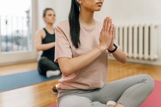 Two women meditate and practice yoga indoors, focusing on mindfulness and relaxation.