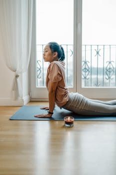 Asian woman practicing yoga indoors near candle, embracing tranquility and focus.