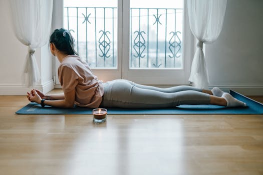 Woman lying on yoga mat indoors, meditating for relaxation and mindfulness.
