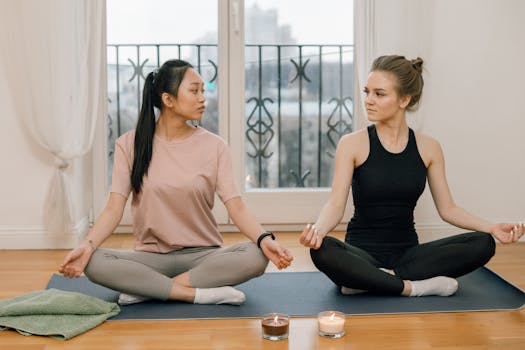 Two women meditating in lotus pose on yoga mats, enhancing mental health.