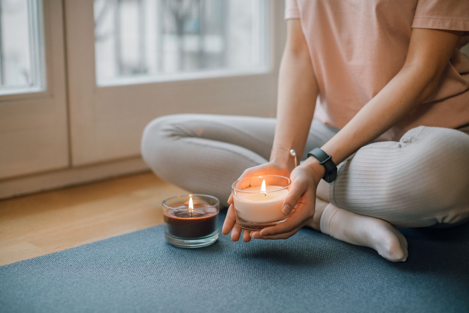 Person seated cross-legged on a yoga mat holding a lit candle during an evening meditation practice