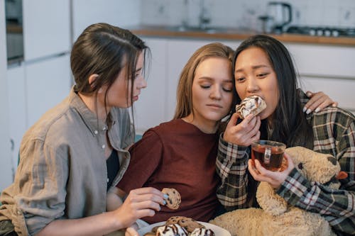 Free Friends Supporting a Sad Young Woman Sitting on a Sofa and Eating Pastry and Drinking Tea Stock Photo