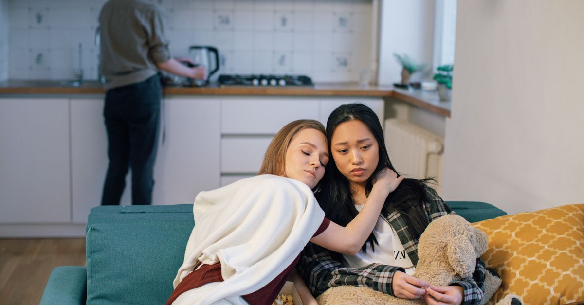 Two women on a couch offering emotional support, indoors.