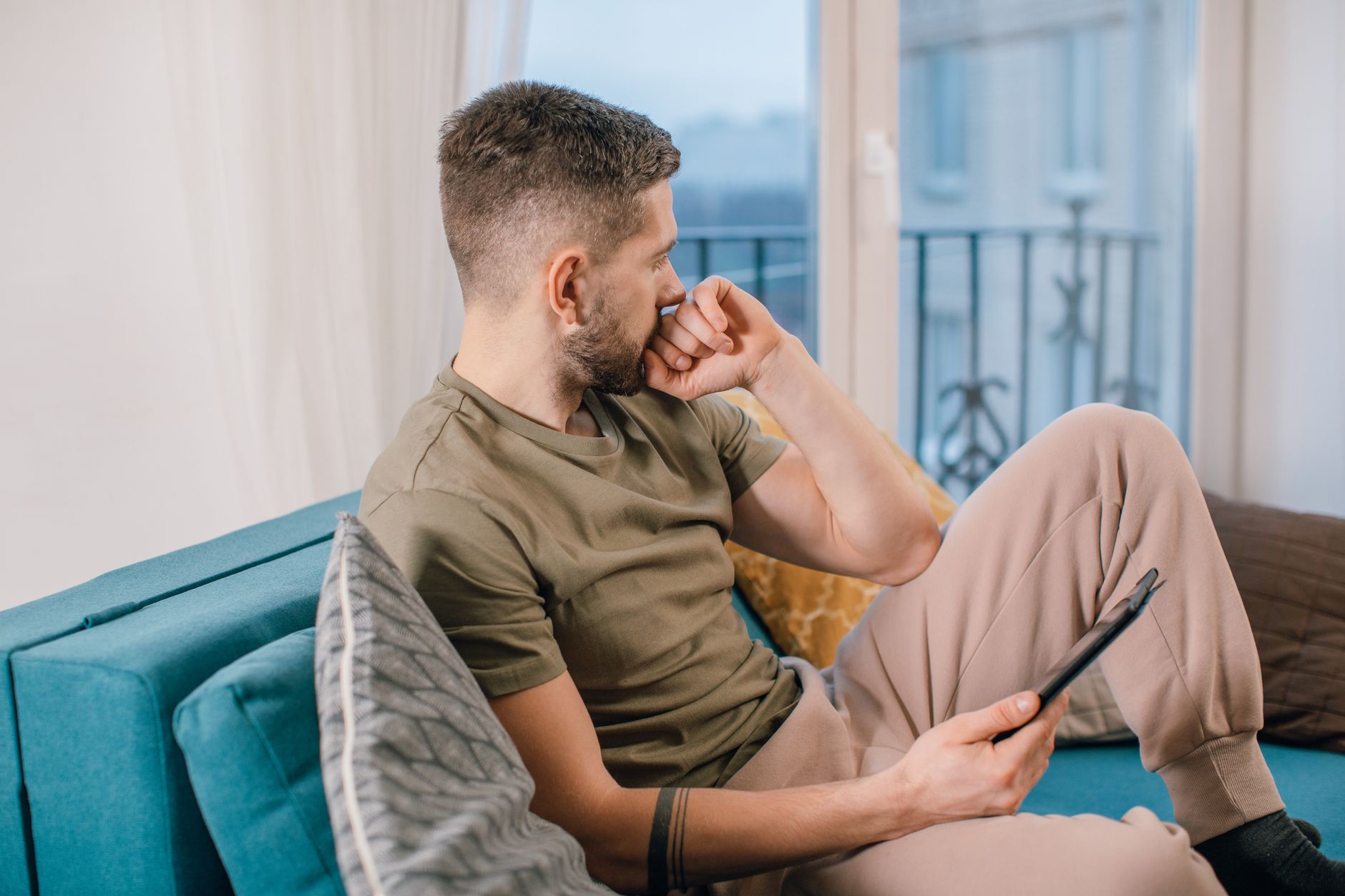 Man met baard zit peinzend op de bank binnenshuis met een tablet.